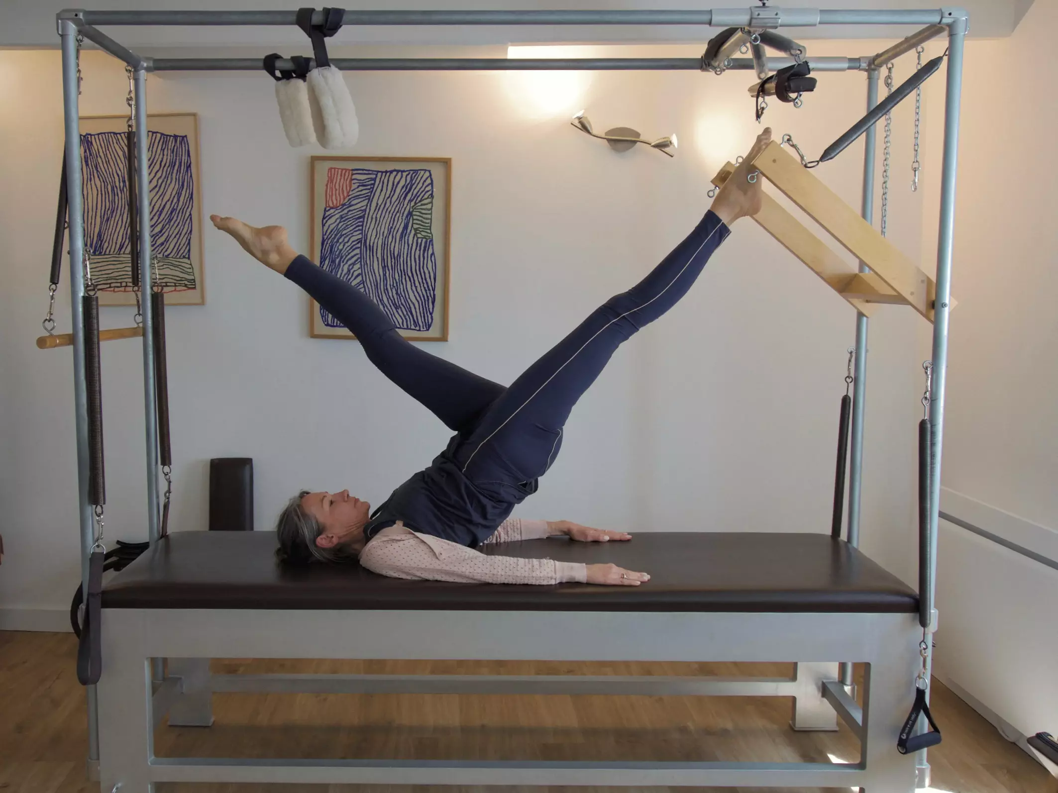 Personne faisant du Pilates sur un appareil avec les jambes levées en l'air.